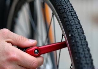 A close-up view of hands using tire levers to remove a flat tire from a bicycle wheel, demonstrating the first step in fixing a puncture.